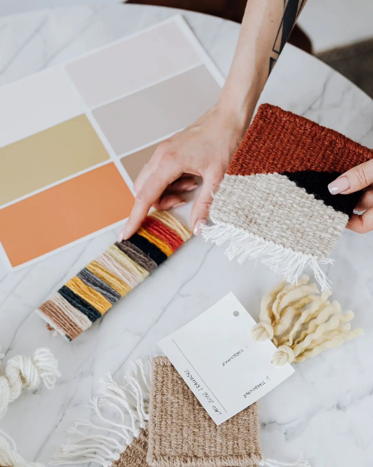 Hands laying out fabric and yarn samples on a marble table