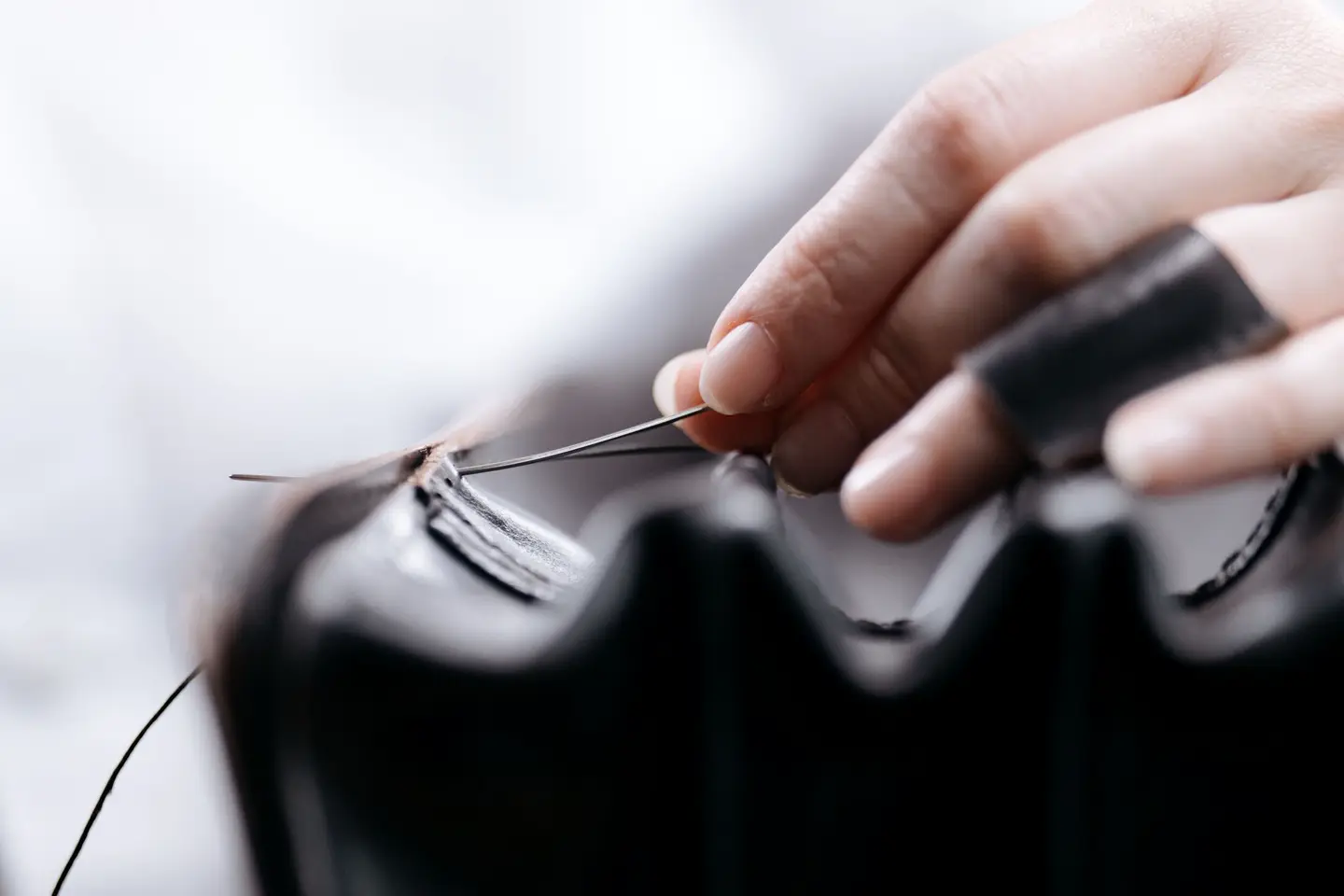 Hands stitching a black leather edge by hand